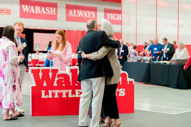 a man and woman hugging in a room with tables and people