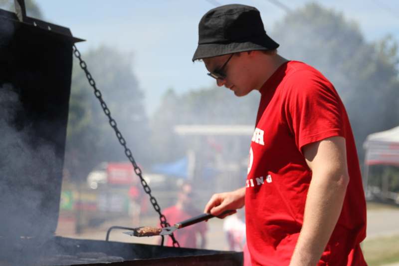 a man in a red shirt and hat cooking meat on a grill