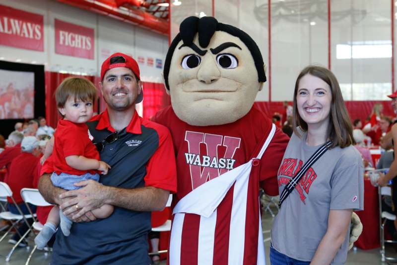 a man holding a child and a mascot posing with a woman