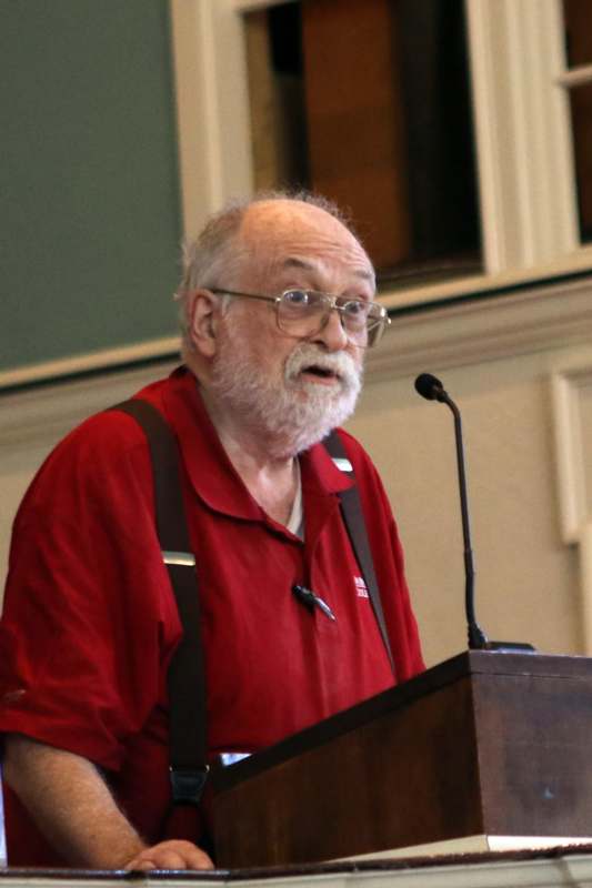 a man in red shirt and suspenders standing at a podium