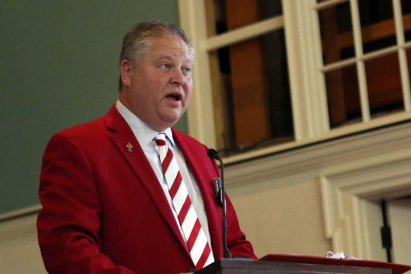 a man in a red suit and tie standing at a podium