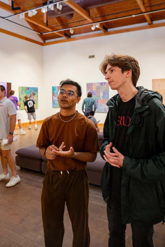 a man standing next to another man in a room with paintings on the wall