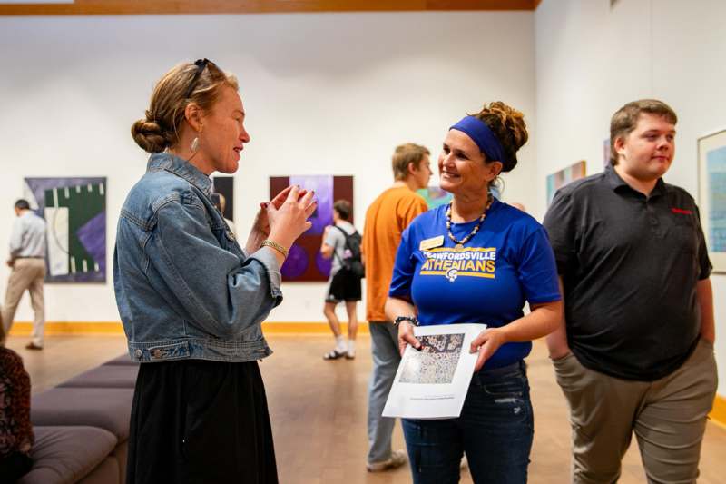 a woman talking to a woman in a room with other people