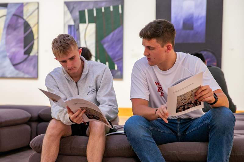 two men sitting on a couch reading books