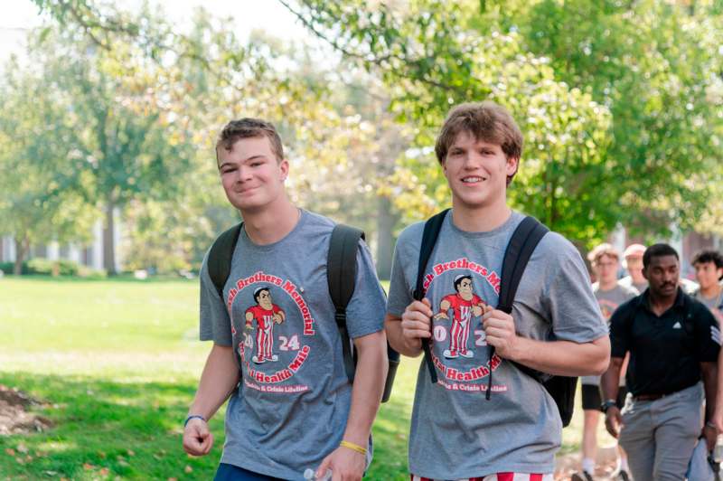 two men wearing backpacks and walking in a park