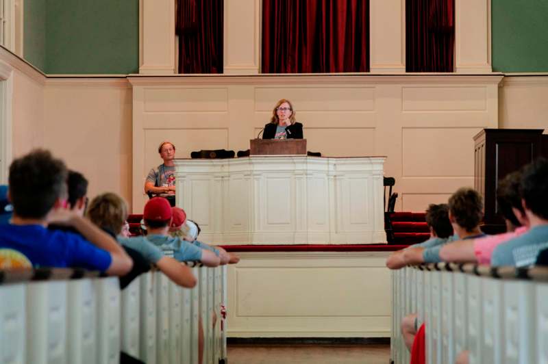 a woman standing at a podium with a group of people in the background