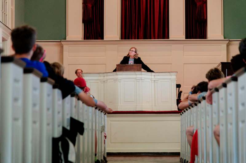 a woman standing at a podium with a crowd of people sitting in chairs