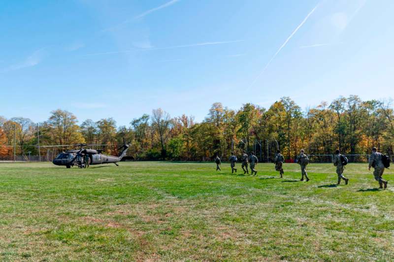 a group of soldiers walking on a grass field with a helicopter