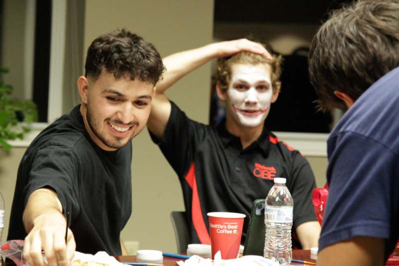 a group of men sitting at a table with a painted face