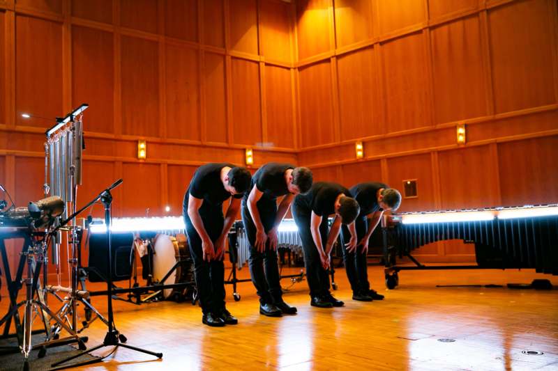 a group of men in black shirts bending over in front of a microphone