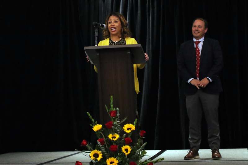 a woman standing at a podium with a microphone and a man in a suit