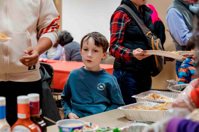 a boy sitting at a table with food in foil trays