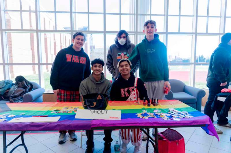 a group of people standing in front of a table with a rainbow flag