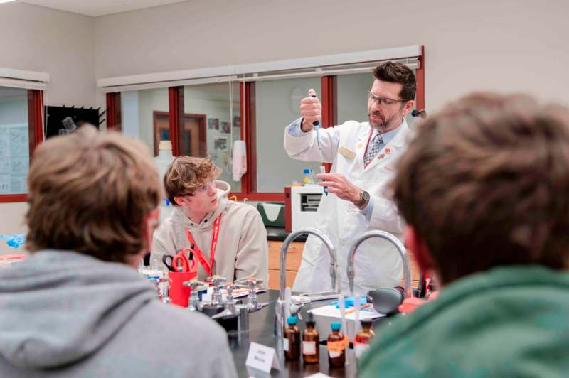 a man in a white coat holding a tube with a test tube in front of a group of people