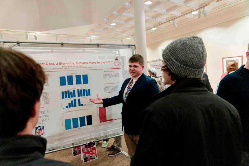 a man standing in front of a white board with a man pointing at a white board with blue and red text