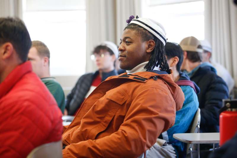 a man in an orange jacket sitting in a classroom