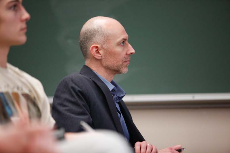 a man in a suit sitting in front of a chalkboard