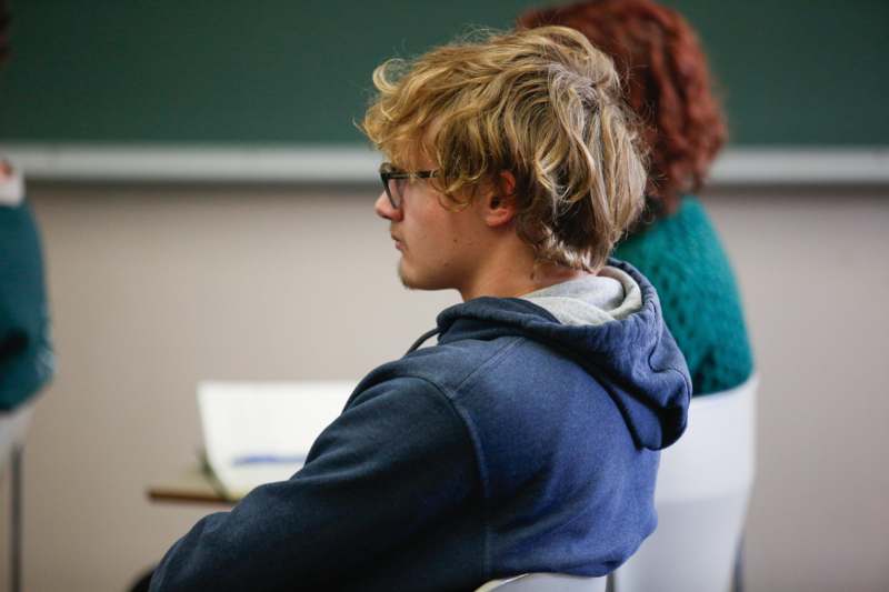 a man in a blue sweatshirt sitting in a classroom