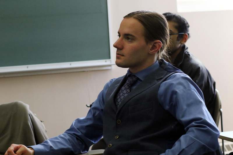 a man in a vest sitting in front of a chalkboard