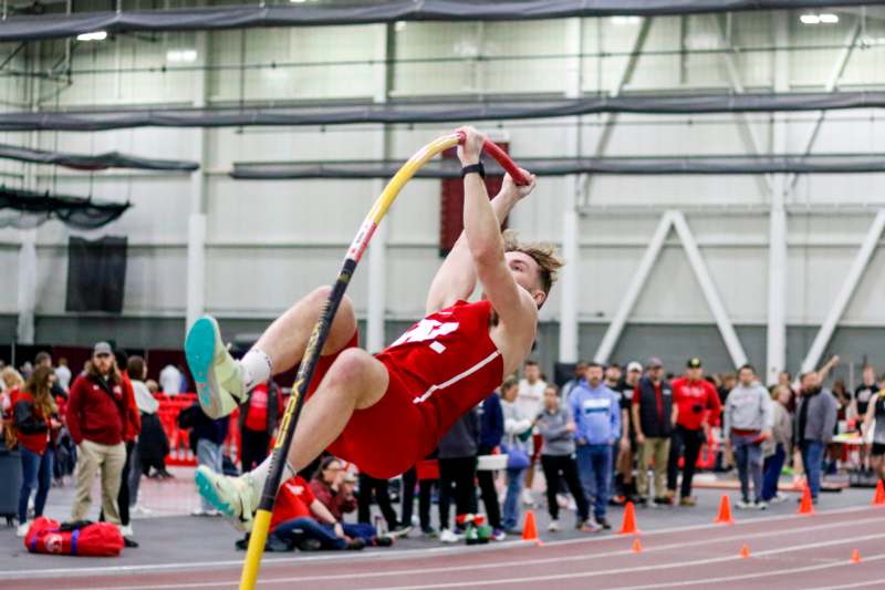 a man in a red shirt jumping over a pole