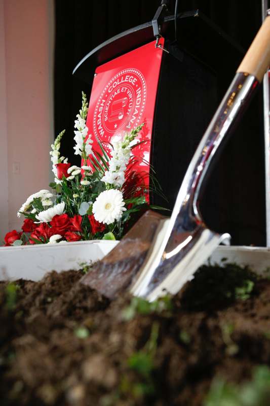 a shovel in dirt with flowers and a red sign