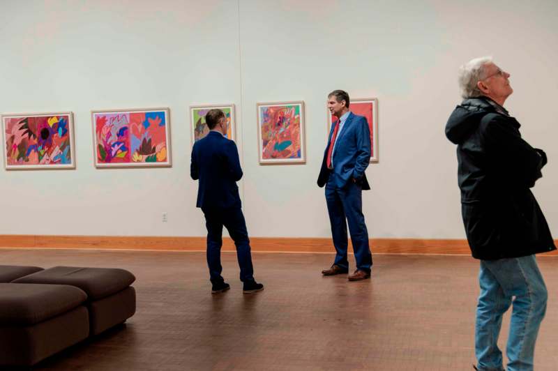 a group of men in suits looking at paintings on a wall