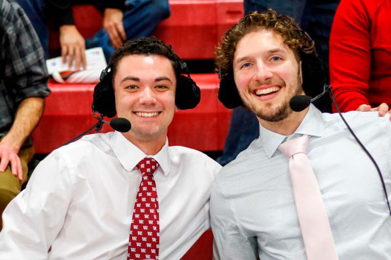 two men wearing headsets and sitting in a stadium