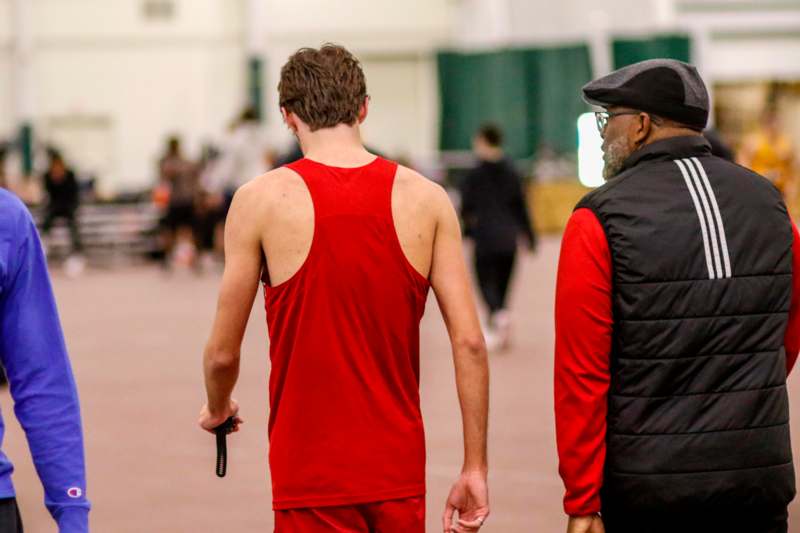 a man in a red tank top and black vest walking away from another man