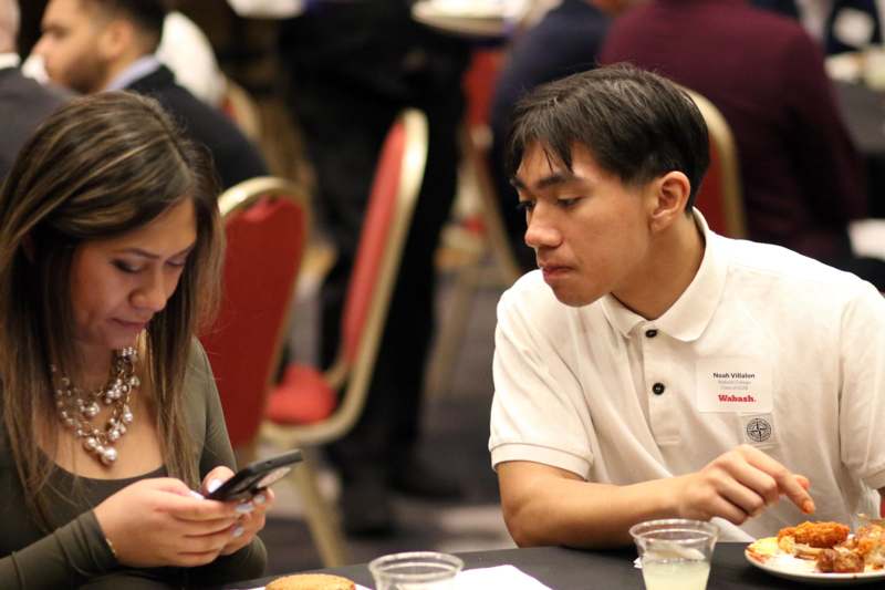 a man and woman sitting at a table looking at their phones