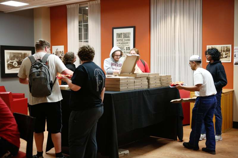a group of people standing around a table with pizza boxes