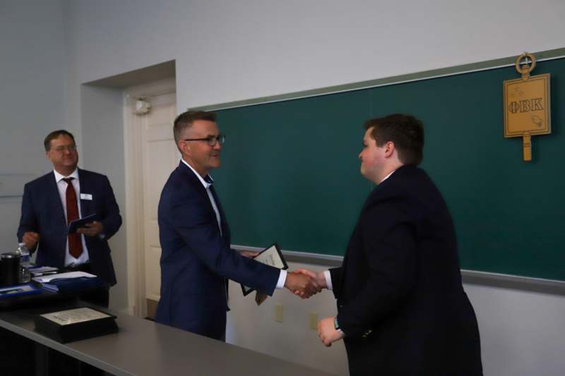 a man in suit shaking hands with another man in a classroom