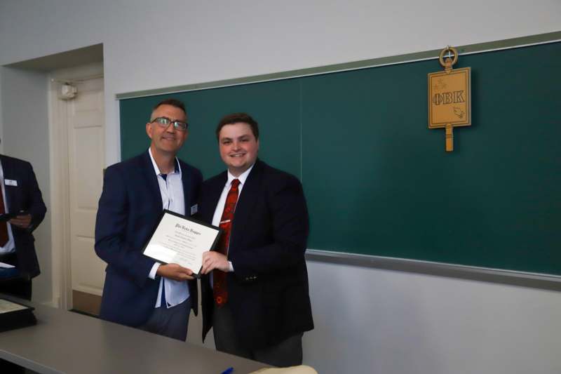 two men in suits holding a certificate in front of a chalkboard