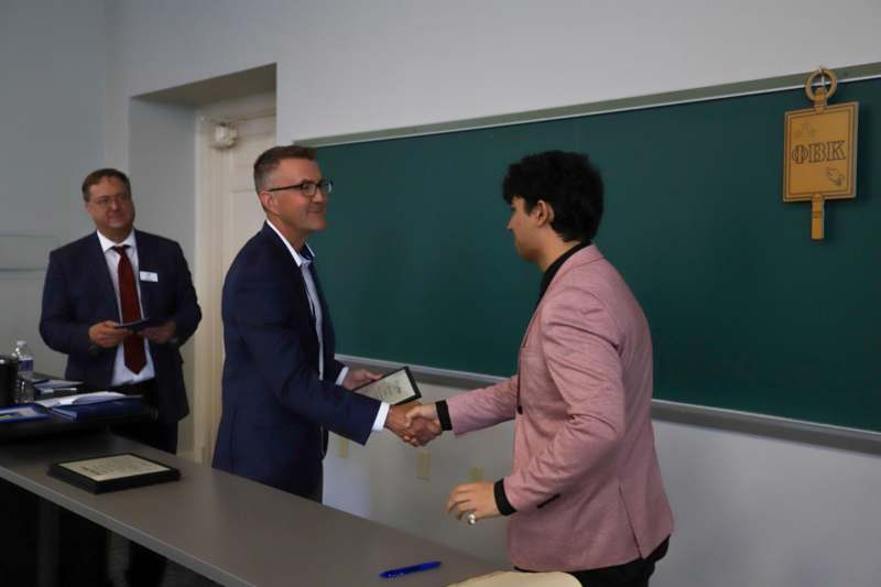 a man shaking hands with another man in front of a chalkboard