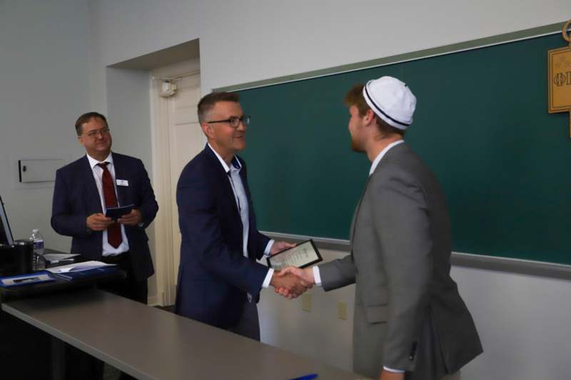 a man shaking hands with another man in front of a chalkboard