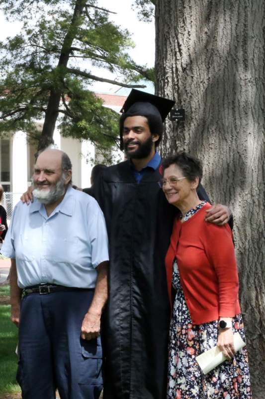 a man in a graduation gown and cap standing next to a man and woman