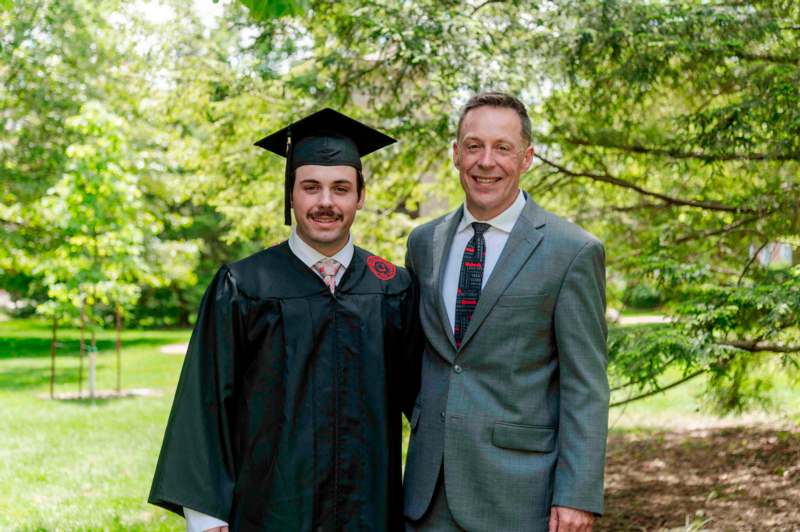 a man in a graduation gown and cap standing next to a man in a suit