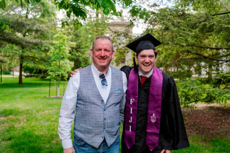 a man in a cap and gown standing next to a man in a graduation gown