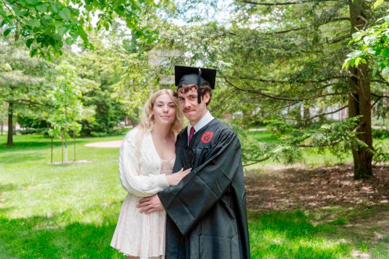 a man and woman in graduation gowns and cap and gown standing in a park