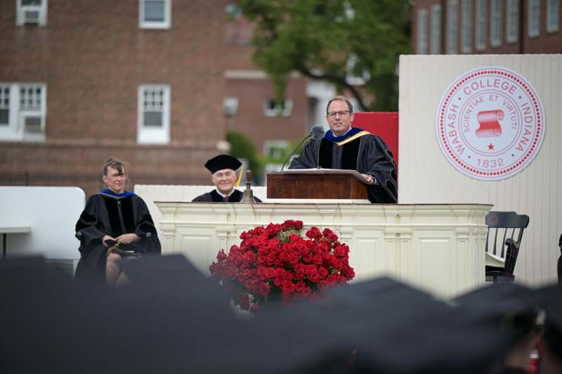 a man in black gowns and cap standing at a podium with a microphone