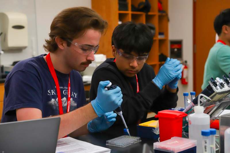 a man wearing goggles and gloves holding a pipette