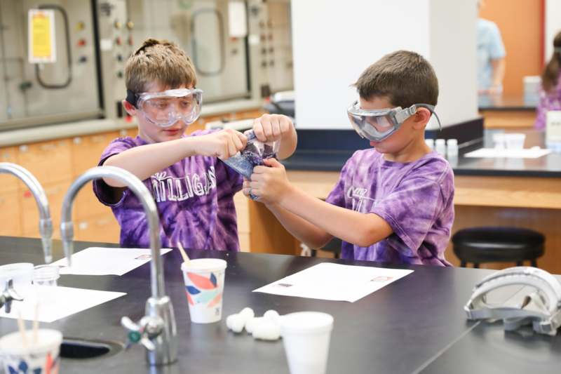 two boys wearing goggles and holding a bag of liquid