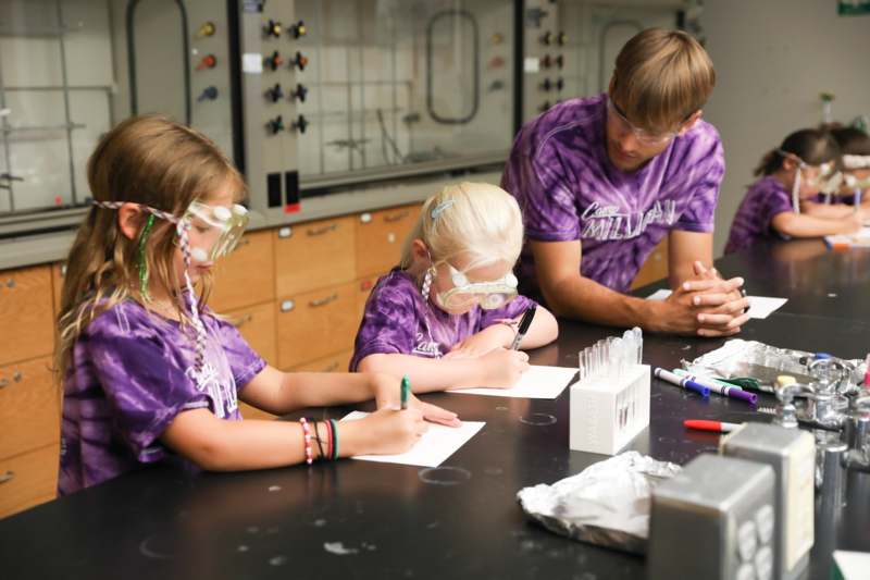 a group of kids sitting at a table writing on paper