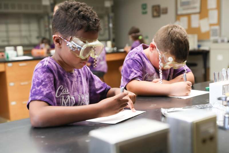 a group of kids wearing safety goggles and writing on paper
