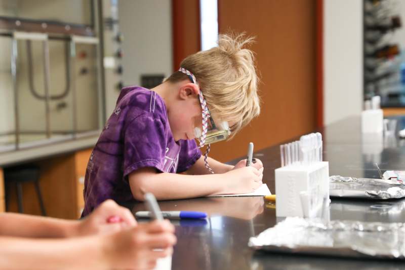 a boy wearing goggles writing on a paper
