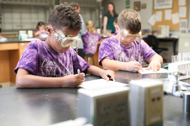 a group of kids wearing safety goggles and writing on paper