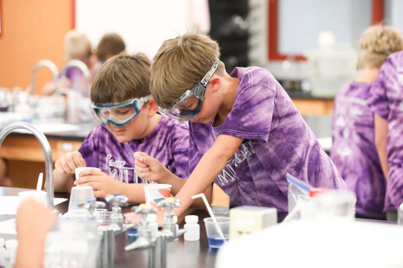 a pair of young boys wearing goggles and standing at a table