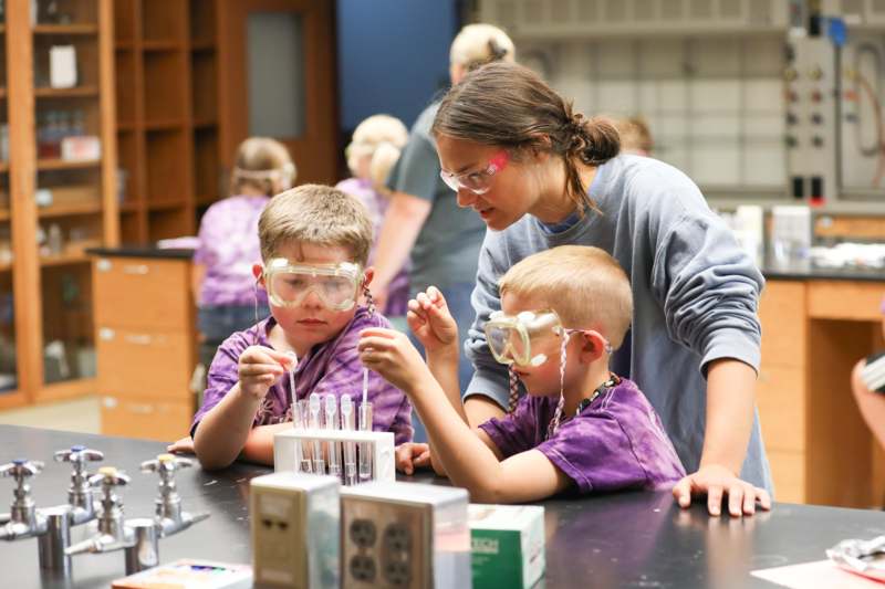 a woman and kids wearing safety goggles and standing at a table