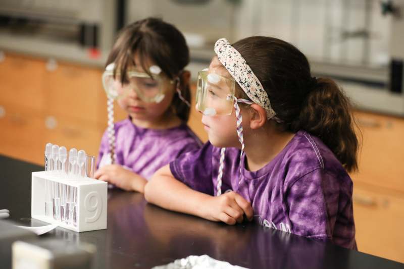two girls wearing safety goggles and looking at a test tube
