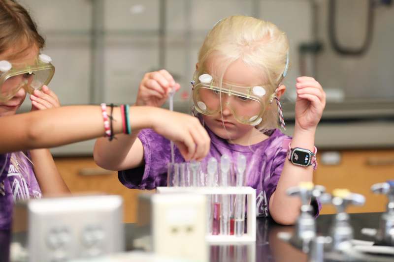 a girl wearing goggles and holding a tube with liquid in it