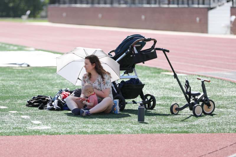 a woman sitting on a field with a baby and a stroller